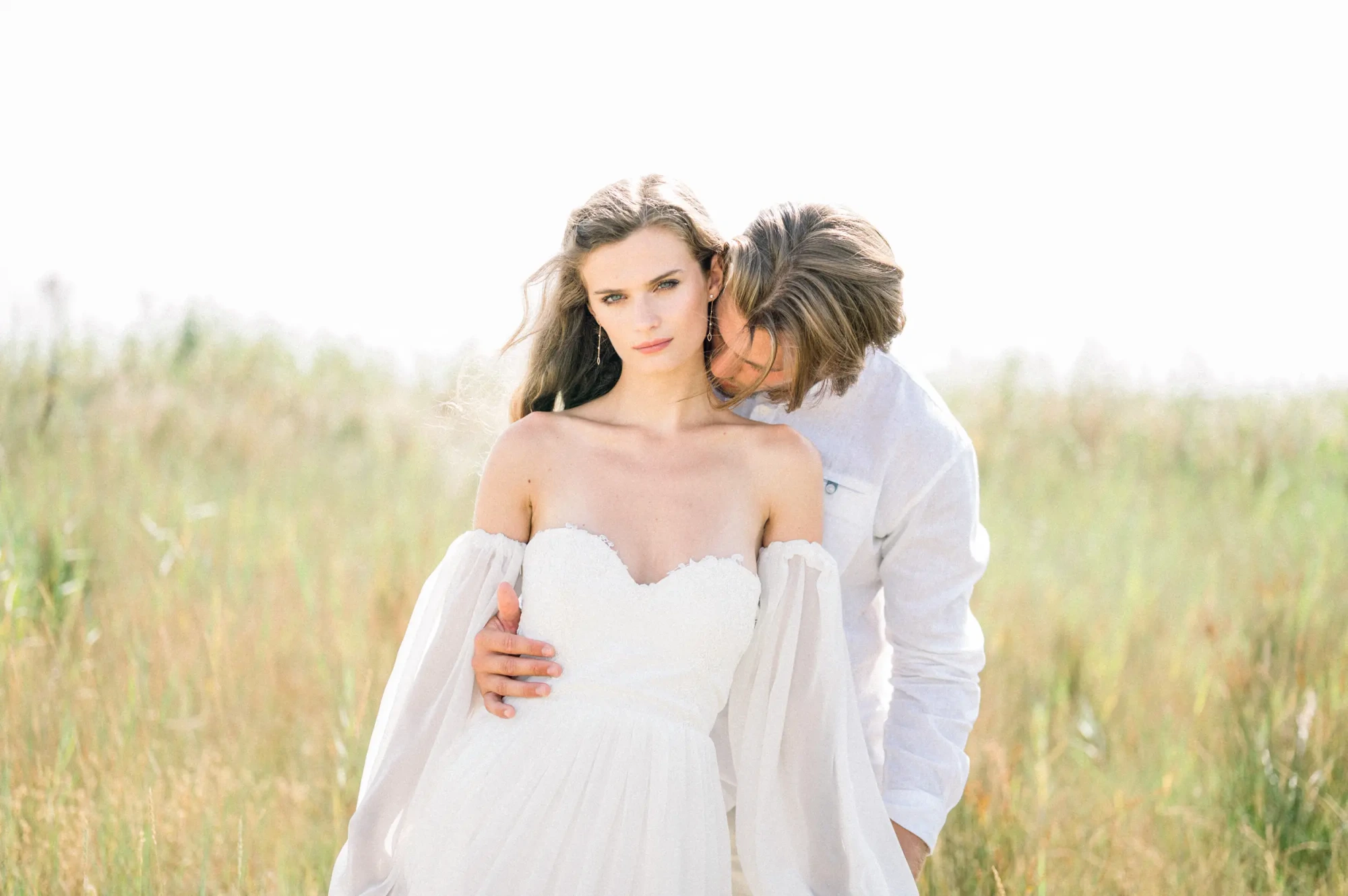 Bride and groom embracing in a field of tall summer grass