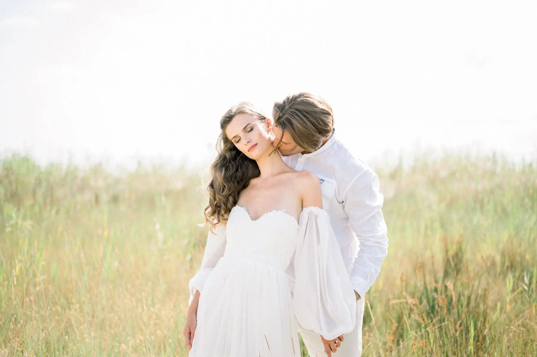 Groom kissing the bride in a summer meadow, wedding videographer in France